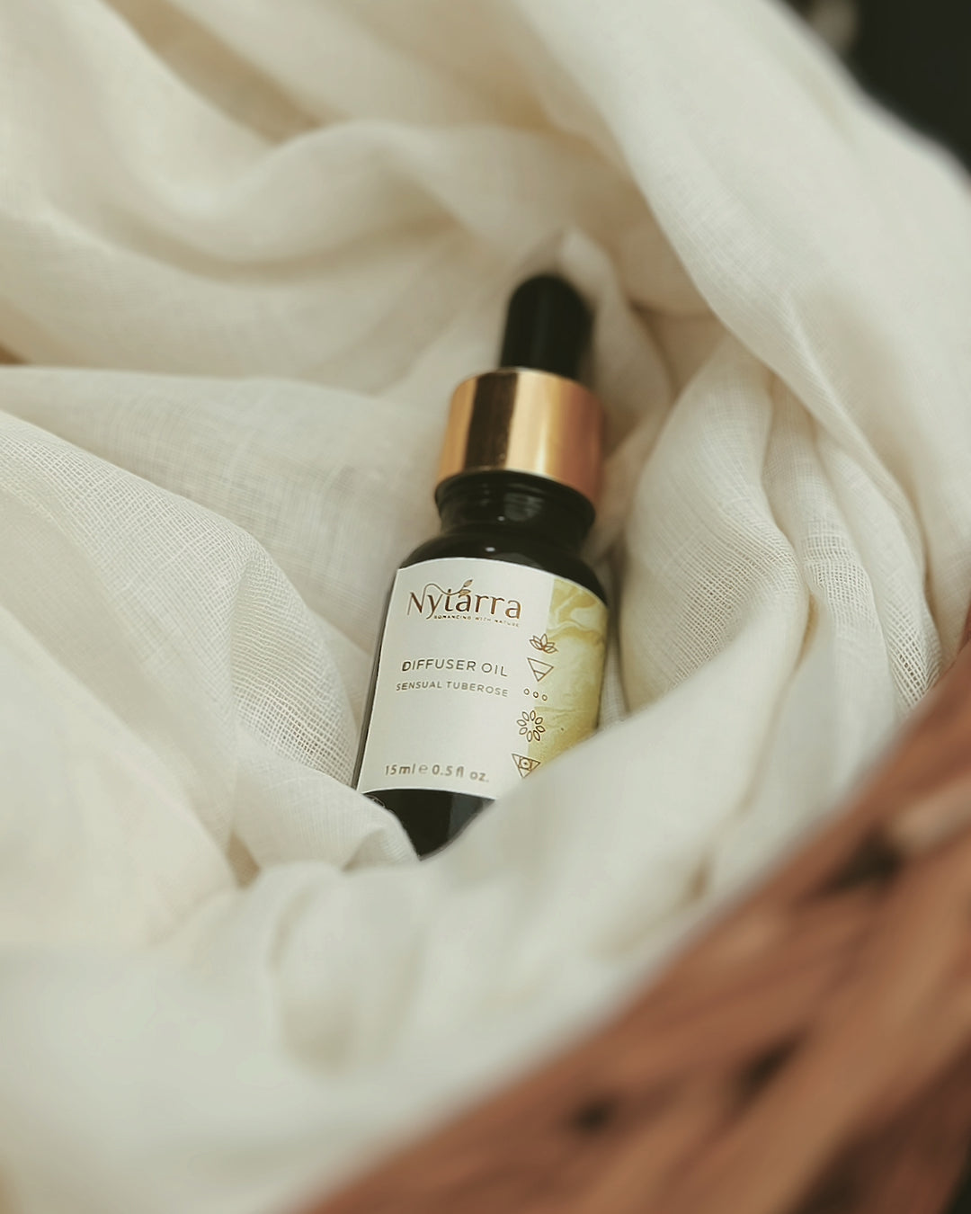 Nytarra Sensual Tuberose Oil – a 15ml amber bottle with a golden dropper releasing fragrant oil, set on a rustic wooden surface.